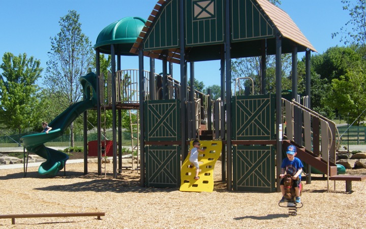 Three kids climbing on Showman's Circle Farm-themed play area at Lake Metroparks Farmpark